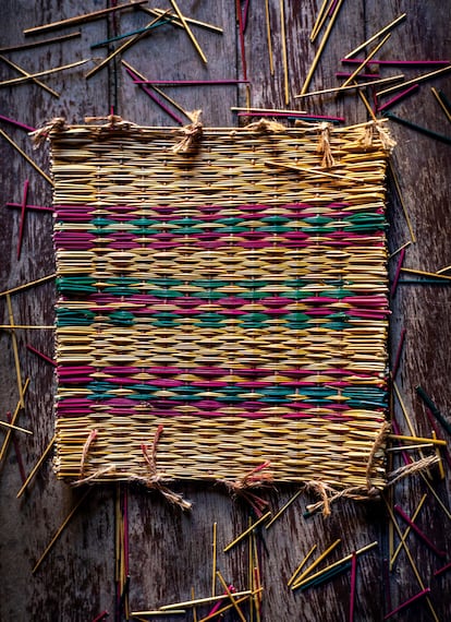 Un 'pedaço', una pieza de junco tejido con colores y diseños tradicionales preparada para ser utilizada como parte lateral de una cesta, junto con los restos de juncos recortados en el telar.