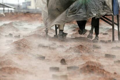 Trabajadores inmigrantes indios se cubren con un plástico mientras el vapor se eleva en un horno de ladrillos, durante las lluvias en las afueras de Katmandú (Nepal).