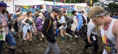 Varias personas caminan por el barro a su llegada al festival británico de Glastonbury en la granja Worthy, cerca de Pilton (Reino Unido), 23 de junio de 2016.