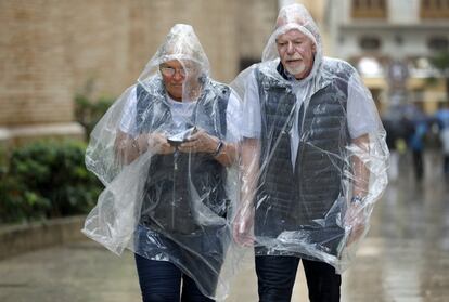 Dos hombres caminan cubiertos con impermeables para protegerse de la lluvia en Valencia.