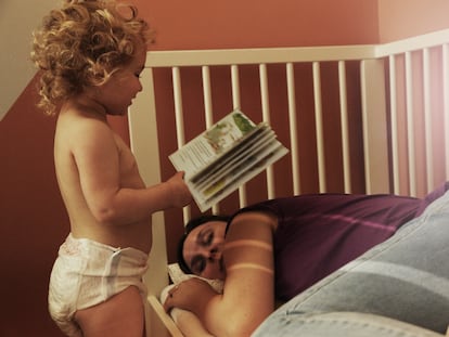 Toddler reading mother a book while she is asleep in a cot