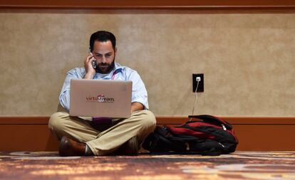 Asistente a la conferencia de seguridad cibernética Black hat usa su móvil y su portátil sentado en el suelo.