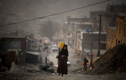 En esta fotografía de archivo del lunes 27 de diciembre de 2010, una mujer carga agua en un recipiente de plástico mientras asciende por una pendiente en el camino hacia su casa en Kabul, Afganistán.