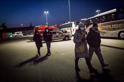 Elzbieta y Tomasz caminan por la noche entre los autobuses del centro comercial de Tesco, en Przemyśl, cerca de la frontera entre Polonia y Ucrania. El centro se ha convertido en punto de acogida inicial para los refugiados que huyen de Ucrania. Los autobuses se dirigen a los diversos destinos de Europa en los que recibirán a los refugiados ucranios. Detrás, Monica camina con Gnako, un activista polaco que llegó a la frontera para colaborar con las actividades de los investigadores.