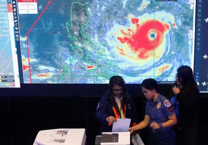 Empleadas del equipo de vigilancia utilizan una fotocopiadora mientras a sus espaldas se muestran detalles sobre el tifón Mangkhut, en el Consejo Nacional de Reducción y Gestión del Riesgo de Desastres en Ciudad Quezón, Filipinas (Manila).