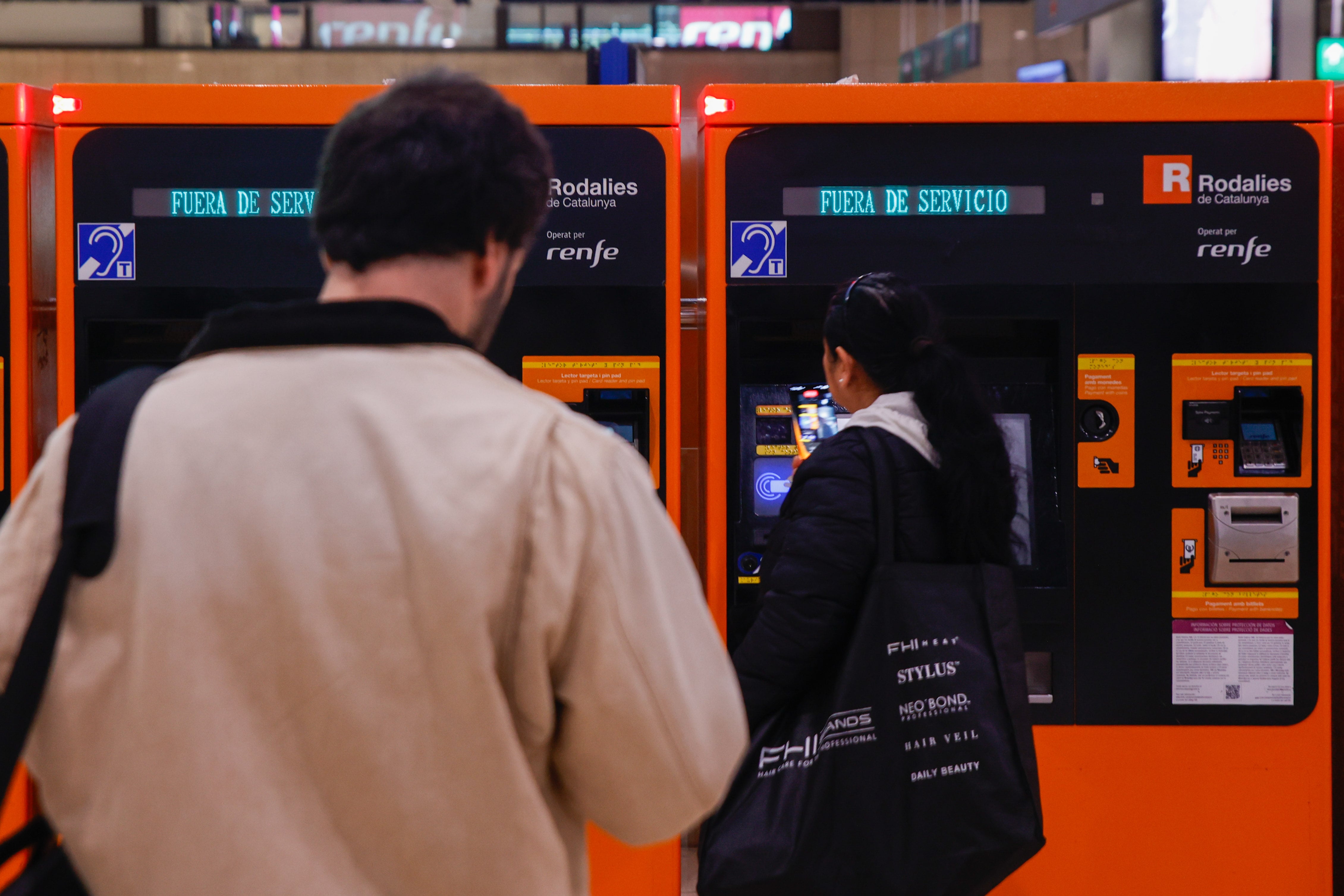 Varias personas observan las máquinas expendedoras de los billetes de Rodalies en la estación de Sants que están fuera de servicio.