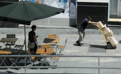 Un hombre, que se protege del sol, mira como otro trabaja en una calle de Madrid.