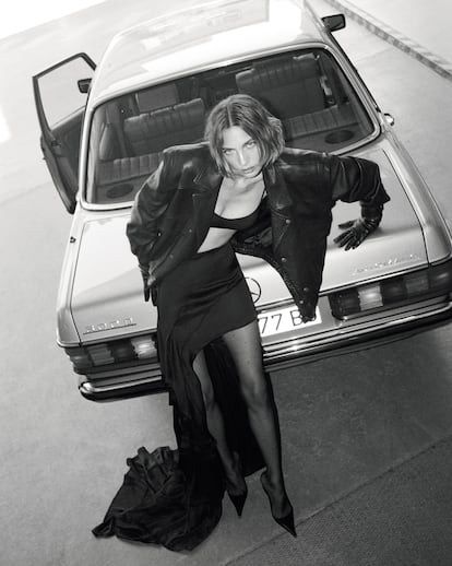 Chaqueta de piel oversize, falda con vuelos asimétrica, medias de puntos, tacón de punta, guantes de piel negros y pendientes plateados, todo de SAINT LAURENT x ANTHONY VACCARELLO.