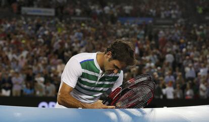 Federer guarda sus raquetas mientras Djokovic se despide del público tras alcanzar la final.