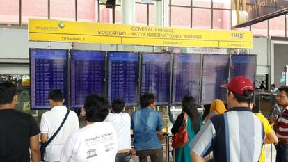 Varios pasajeros consultan los detalles de sus vuelos en una pantalla en un aeropuerto. 