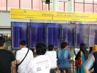 Varios pasajeros consultan los detalles de sus vuelos en una pantalla en un aeropuerto. 