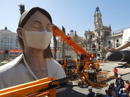 Operarios colocan una mascarilla a la falla del Ayuntamiento, este miércoles en Valencia.