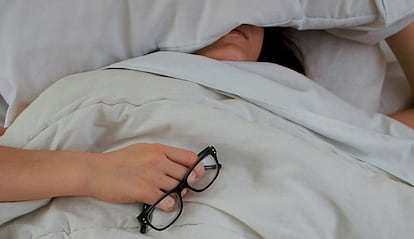 Chica durmiendo en una cama con unas gafas en la mano