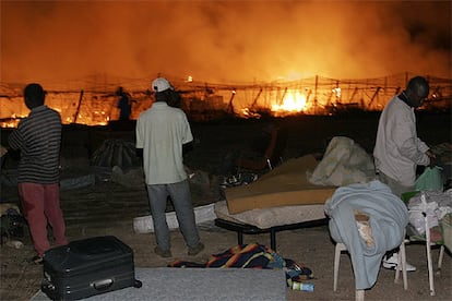 Varios inmigrantes contemplan el fuego entre sus pertenencias.