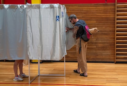 Un hombre lleva a su perro en una mochila mientras entra a una cabina para emitir su voto en la segunda vuelta de las elecciones parlamentarias francesas.