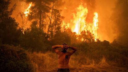 Homem observa um grande incêndio florestal que se aproxima da aldeia de Pefki na ilha de Evia (Eubeia), a segunda maior ilha da Grécia, neste domingo.