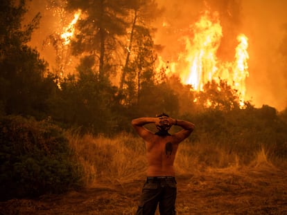 Homem observa um grande incêndio florestal que se aproxima da aldeia de Pefki na ilha de Evia (Eubeia), a segunda maior ilha da Grécia, neste domingo.