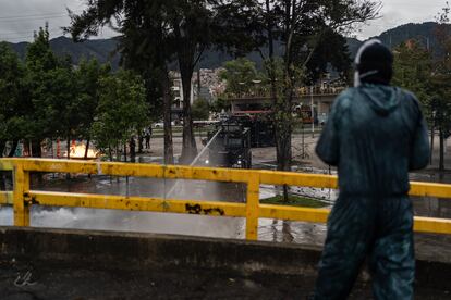 Un manifestante observa desde la parte superior de la entrada a la universidad la respuesta de la Policía. Algunos estudiantes se quejan del uso de agua para dispersarlos. “Hay racionamiento en Bogotá y ellos usan el agua como un arma”, dice uno de ellos. “¿Si viste la cantidad de agua? Y luego no hay en casa”, afirma otra estudiante. 
