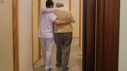 Un auxiliar ayuda a una persona mayor en un centro de día de Sevilla.