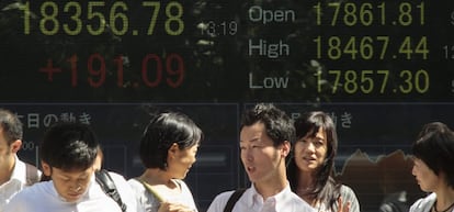 Peatones caminan frente a una pantalla que muestra informaci&oacute;n burs&aacute;til en Tokio .