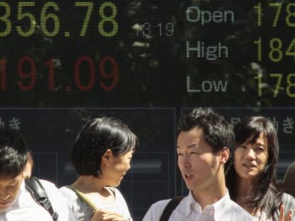 Peatones caminan frente a una pantalla que muestra informaci&oacute;n burs&aacute;til en Tokio .