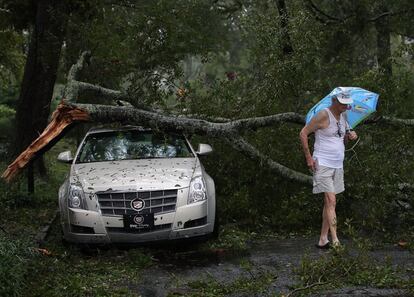 Un vecino de la ciudad de Wilmington (Carolina del Norte) camina junto a su coche dañado por una rama, el 16 de septiembre.