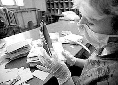 Una empleada de correos revisa con guantes y mascarilla unos sobres.