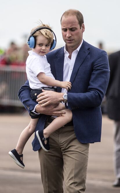 El príncipe Jorge ha cruzado parte de la pista aérea en brazos de su padre, Guillermo de Inglaterra, y llevando unos cascos aislantes especiales para un niño de su edad.