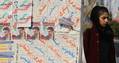 Una mujer iran&iacute; junto a los carteles electorales para los comicios de marzo.
