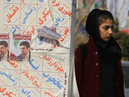 Una mujer iran&iacute; junto a los carteles electorales para los comicios de marzo.