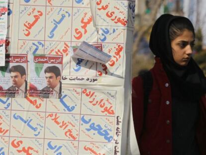 Una mujer iran&iacute; junto a los carteles electorales para los comicios de marzo.