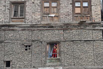 Una mujer de Kashmiri (India) mira por la ventana de su casa.