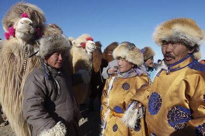 Tres personas con trajes mongoles junto a sus camellos.