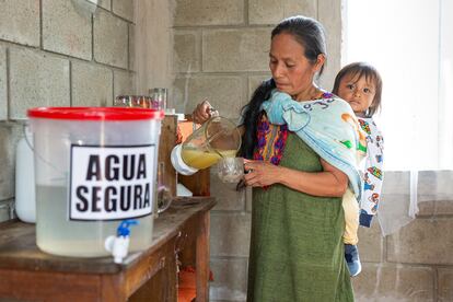 Olga Ascensios, de la comunidad de Quimotari (Perú), prepara un zumo saludable junto a su bidón de agua potable y con su hijo a la espalda.