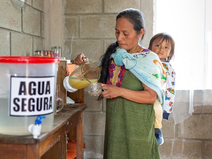Olga Ascensios, de la comunidad de Quimotari (Perú), prepara un zumo saludable junto a su bidón de agua potable y con su hijo a la espalda.