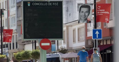 Dos personas protegidas con mascarilla pasean bajo una banderola electoral del PSdeG en Foz, en la comarca de A Mariña, Lugo, Galicia