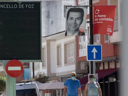 Dos personas protegidas con mascarilla pasean bajo una banderola electoral del PSdeG en Foz, en la comarca de A Mariña, Lugo, Galicia