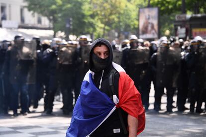 Um manifestante mascarado e coberto com a bandeira nacional francesa na frente de um grupo de policiais.