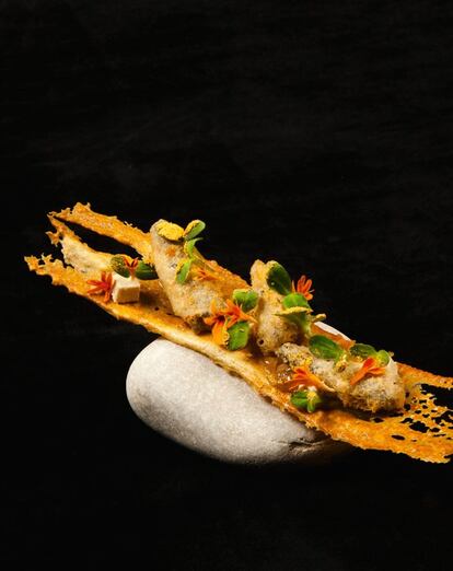 <p><b>Ingredientes: </b> 8 galletas de pan, 24 sardinas con tempura, dados de mayonesa de anchoas, cebolla confitada, germinado de pepino, hojas de tagete. Para la galleta de pan: 50 gramos de miga de pan blanco, 5 de harina de trigo, 60 de claras de huevo, pimienta, sal. Para la cebolla confitada: 30 gramos de escalonia picada y limpia, 30 de cebolla blanca picada y limpia, 30 de aceite de pepita de uva, 10 de vinagre de escalonia, 25 de almíbar, aceite de oliva, sal y pimienta. Para la mayonesa de anchoas: 65 gramos de mayonesa, 2 de mostaza de Dijon, 12 de anchoas, 2 de alcaparras, 5 de aceite de pepita de uva, 6 de nata, 30 de nata, 1 de agar agar, 2 hojas de gelatina. Para las sardinas en tempura: 100 gramos de tempura japonesa, 170 de agua, 24 sardinas pequeñas de lata en aceite, aceite de semilla, harina de trigo. <p><b>Preparación:</b> 1. Galleta de pan: poner pan, harina, sal y pimienta en un robot. Triturar durante 4 minutos. Añadir las claras y triturar 1 minuto a menor velocidad hasta tener una pasta homogénea. Extender sobre una placa siliconada y hornear 10 minutos a 130º C. Reservar. 2. Cebolla confitada: freír las cebollas en aceite de oliva. Cuando empiece a dorar, mojar con el vinagre de escalonia y dejar unos minutos. Agregar el almíbar, salpimentar y reducir. 3. Mayonesa de anchoas: triturar con una varilla eléctrica la mayonesa, la mostaza, las anchoas, las alcaparras, el aceite y la nata. Reservar. En un robot de cocina, poner la nata con el agar-agar. Llevar a 90º C y luego bajar la temperatura a 45º C. Remojar las hojas de gelatina y agregarlas. Batir y agregar el primer preparado hasta tener una crema homogénea. Verter en una placa y congelar. Cortar en dados. 4. Sardinas en tempura: mezclar la tempura con agua muy fría y reservar en frío. Pasar las sardinas por la harina y la tempura. Freír en aceite de semilla. Reservar. 5. Presentación: colocar la galleta sobre un plato y poner tres puntos de cebolla confitada. Encima van las sardinas, la mayonesa, las hojas de mostaza y las flores.