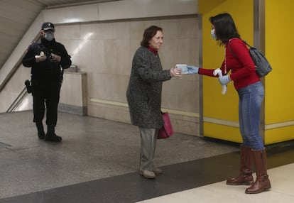 Un agente de la Policía Nacional vigila el reparto de mascarillas de una voluntaria de la Cruz Roja, en la estación de metro de Avenida de América de Madrid el 13 de abril.