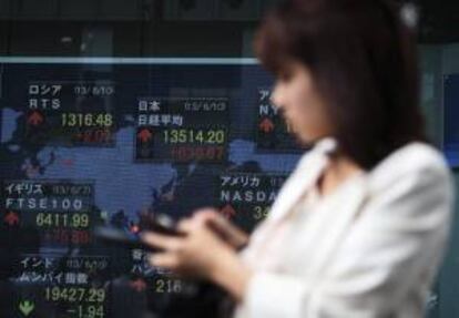 Una mujer camina junto a una pantalla que muestra información bursátil en Tokio (Japón). El índice Nikkei de la Bolsa de Tokio abrió hoy con una subida de un 2,61 por ciento. EFE/Archivo