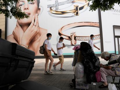 Un grupo de personas pasa junto a una mujer que recoge materiales reciclables en la calle comercial de Wanfujing en Pekín este miércoles