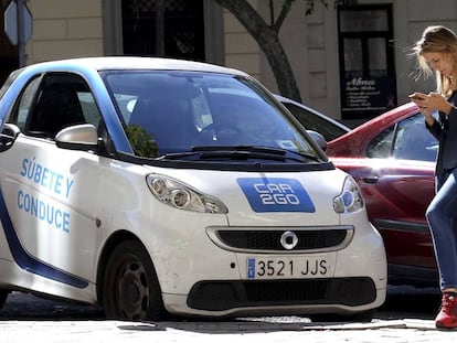 Una usuaria consultando su m&oacute;vil junto a un coche de Car2Go.