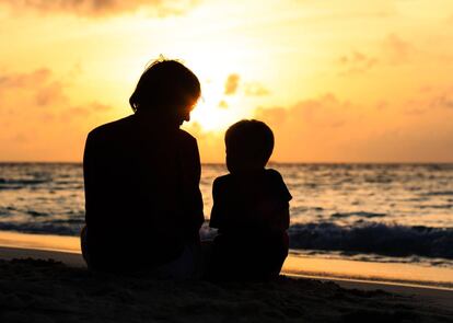 Padre y su pequeño hijo mirando al atardecer en la playa.