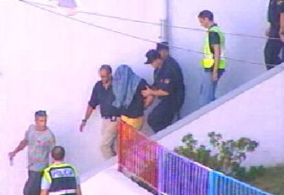 Imagen de la televisión que muestra al detenido acompañado por la policía a la salida de su domicilio.