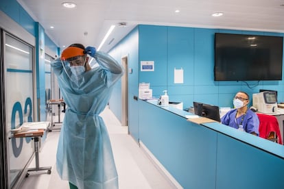 En febrero de 2021, el hospital Ramón y Cajal inauguró la nueva Unidad de Cuidados Intensivos (UCI). Tiene 24 camas, ventana en todos los boxes y vigilancia del paciente permanente mediante una cámara, además de ventilación mejorada. En la imagen, un celador se coloca un equipo de protección individual (EPI) antes de entrar en uno de los habitáculos el viernes 5 de marzo. Le mira el técnico de cuidados auxiliares de enfermería (TCAE) Juan de Dios García. Toda la unidad estaba ocupada por enfermos de coronavirus.