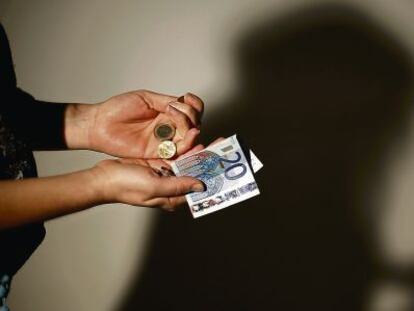 Las manos de un joven con un billete de 20 euros y varias monedas.