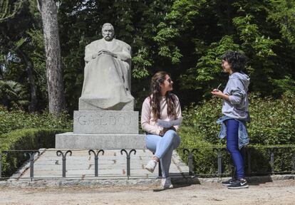 Dos jóvenes charlan junto a la estatua de Benito Pérez Galdós, en el parque del Retiro.
