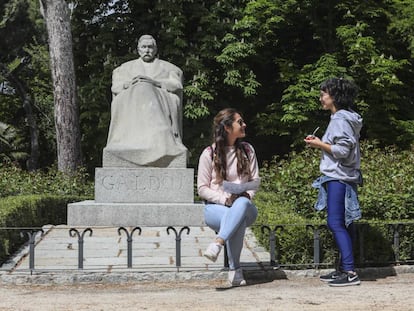 Dos jóvenes charlan junto a la estatua de Benito Pérez Galdós, en el parque del Retiro.