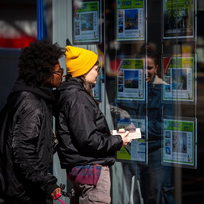 Dos jóvenes consultan el escaparate de una inmobiliaria.